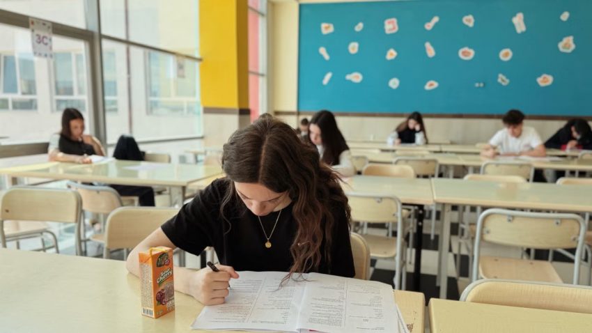 Student concentrated on exam in classroom setting with natural light.